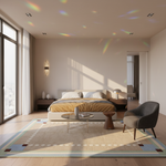 A modern, sunlit bedroom with a beige upholstered bed, mustard yellow bedding, a gray armchair, a round glass coffee table, and a patterned beige rug. Sunlight streams through large windows, casting rainbow light patterns across the ceiling and floor.