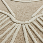 Close-up of a textured beige rug with a raised cream-colored geometric sunburst pattern.