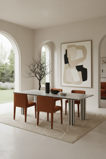 A modern dining room scene featuring a rectangular table with a white and black striped top and striped legs, surrounded by four brown upholstered chairs on a patterned beige rug. The room has warm neutral walls, arched windows, and a large abstract art print on the wall.