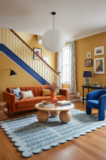 Living room with orange sofa, blue scallop hand made rug, armchair, and wooden coffee table.