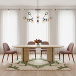 A modern dining room scene featuring a light wood oval dining table with three blush pink upholstered chairs, a contemporary multi-arm chandelier with colorful glass globes, and a patterned cream rug on a light wood floor.