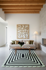 A modern living room featuring a prominent black and white geometric striped rug with a scalloped edge, styled with a wooden coffee table, a beige sofa, and a large abstract canvas print on the wall.