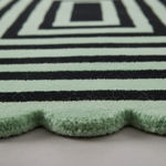Close-up of a plush rug with horizontal mint green and black stripes and a scalloped edge, shown on a neutral surface.