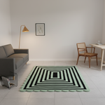 A rectangular area rug with a mint green border and concentric black geometric stripes, styled in a minimalist modern living room with a gray sofa, wooden chair, and floor lamp.