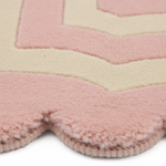 Close-up of a plush, scalloped-edge rug with concentric chevron patterns in dusty pink and cream.
