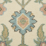 Close-up of a patterned rug with a cream background and a central floral medallion in light blue, dusty pink, sage green, and dark brown.