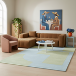 A styled living room scene featuring a large brown sectional sofa, a matching accent chair, a light blue and pale green area rug, a white coffee table, and a colorful framed painting on the wall.