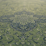 A close-up view of a green area rug with a traditional medallion pattern in dark blue-gray and beige tones, shown in a shallow depth of field.