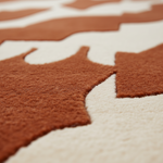Close-up of a textured area rug with a terracotta rust and cream abstract organic pattern.