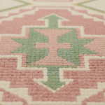 Close-up of a textured rug with a geometric pattern in dusty pink, sage green, and cream.