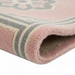 A close-up of a folded area rug showing its pink plush pile, cream and gray striped border, and textured multicolor backing.