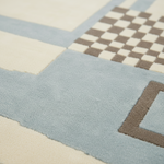 Close-up of a textured area rug with a geometric pattern featuring a large light blue block, cream sections, and a brown-and-cream checkerboard motif.