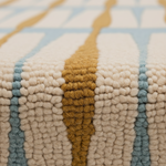 Close-up of a textured woven rug with a geometric pattern in cream, mustard yellow, and light blue.
