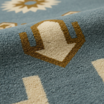 Close-up of a textured area rug featuring a geometric cactus motif in tan and cream on a dusty blue background.