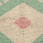 Close-up of a textured cream-colored rug with a central dusty pink diamond pattern and a mint green border.