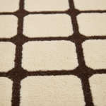 Close-up of a plush area rug with a geometric pattern of cream-colored rounded squares separated by dark brown grid lines.