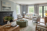 Living room with gray rug, sofa, armchairs, and ottoman in a well-lit room with large windows.