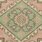 A close-up of a traditional patterned rug featuring a central diamond medallion in sage green, dusty pink, and cream with dark gray accents.