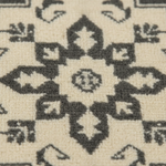 Close-up of a textured area rug featuring a cream-colored base with a dark charcoal gray geometric medallion pattern.