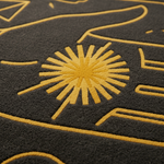Close-up of a dark charcoal gray textured rug with a mustard yellow abstract sunburst and line pattern.