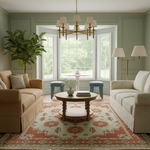 A beautifully styled living room featuring a tan slipcovered sofa on the left, a textured cream bouclé sofa on the right, a round wooden coffee table, a large red and beige patterned area rug, and a tall potted fiddle-leaf fig plant near the bay window.