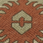 Close-up of a textured woven rug with a rust orange field and a central diamond motif in light beige outlined with dark brown stitching.