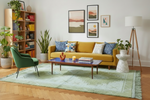 Living room with yellow sofa, green rug, and decorative elements.