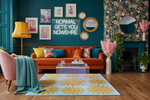 Modern living room with orange sofa, pink armchair, sun rug, and decorative elements.