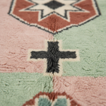 Close-up of a textured, plush area rug with a southwestern geometric pattern in dusty pink, sage green, terracotta, and charcoal gray.