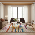 A brightly lit living room with a large colorful area rug, two dark armchairs, a sofa, a coffee table, and a wooden chair in front of tall windows with white curtains.