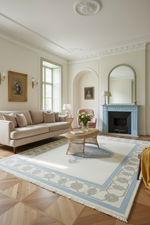 A styled living room featuring a large cream and light blue patterned area rug on a wood parquet floor, with a beige sofa, a wicker coffee table, and a light blue fireplace in the background.