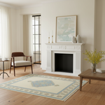 A cream and light blue area rug with a central medallion and floral border, styled in a bright, modern living room with a white fireplace, wooden floor, and side tables.