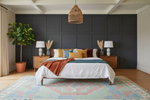 Modern bedroom with tribal green knotted rug, dark paneled walls, a bed with colorful pillows, and decorative elements.
