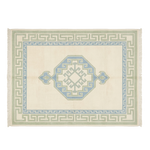 A rectangular woven rug with a cream background, featuring a central light blue octagonal medallion, Greek key borders in sage green and light blue, and fringe on the short ends.