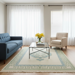 A large rectangular area rug with a Greek key border and central medallion design in cream, sage green, and light blue, styled in a bright living room with a blue sofa, beige armchair, and glass coffee table.