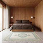 A modern bedroom with wood-paneled walls and ceiling, featuring a low wooden bed with brown bedding and a rectangular area rug in cream, blue, and green tones. Large windows with white curtains are on the left, and wall-mounted round lamps sit on either side of the bed.