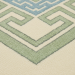 Close-up of a textured area rug with a geometric Greek key pattern in sage green, cream, and light blue.