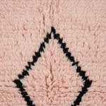 Close-up of a soft, textured pink rug with a black geometric diamond border pattern.