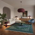 A styled living room interior with a large green patterned area rug on herringbone wood flooring, a white sectional sofa, a blue accent chair, mushroom-shaped table lamps, and a burgundy pendant light.
