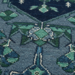 Close-up of a patterned rug with a geometric and floral design in shades of slate blue, teal, green, and cream.