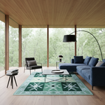 A modern living room with a blue sectional sofa, black accent chair, glass coffee table, and a green patterned area rug. Large floor-to-ceiling windows reveal a dense green forest outside, and the room has light wood ceiling and flooring.