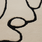 Close-up of a textured area rug with a cream background and a thick black abstract line pattern.