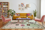Modern living room with yellow sofa, pink chairs, and decorative rug.