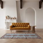 A mustard yellow tufted velvet loveseat sofa in a modern, minimalist room with light wood floors, a patterned rug, and a white fireplace mantel.