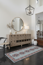 entryway room with wooden dresser, round mirror, and patterned rug.