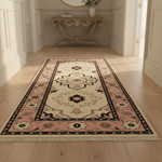 A rectangular area rug with a traditional medallion pattern in beige, pink, and black, shown on a light wood floor in a bright, elegant hallway.