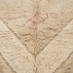 Close-up of a plush, textured fleece blanket in a warm beige color, featuring a central diamond pattern with a small pink embroidered star.