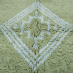 Close-up of a plush, textured bath mat in sage green with a raised diamond pattern in a contrasting pale blue-gray.