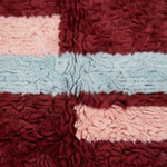 Close-up of a textured, loop-pile rug with a patchwork design in burgundy, dusty pink, and light blue.