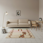 A modern living room scene featuring a beige sofa, a patterned area rug with geometric and tribal-inspired motifs, a wooden chair, a floor lamp, and a desk against a warm taupe wall.